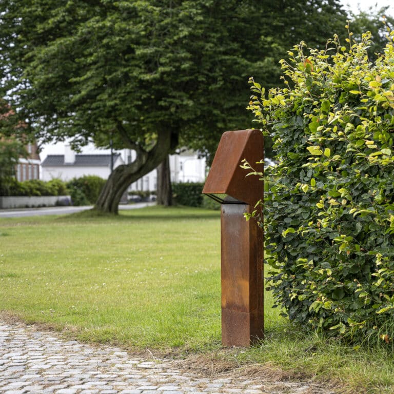 Rusten lampe ved en grøn busk i parken