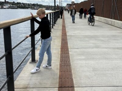 Barn ved rælingen på en promenade nær vandet.