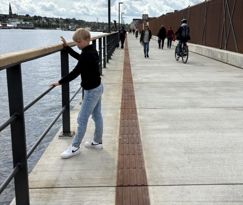 Barn ved rælingen på en promenade nær vandet.