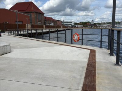 Havnepromenade med livredderbøje og skyer