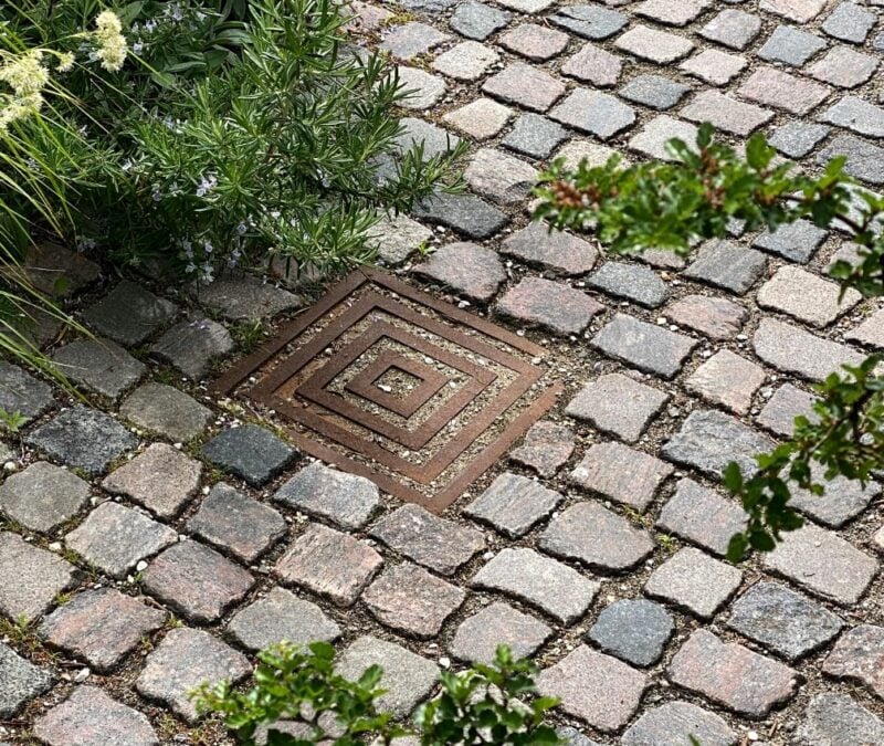 Gadebelægning med brønddæksel og planter