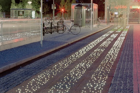 Oplyst fortov med cykler og buskure.