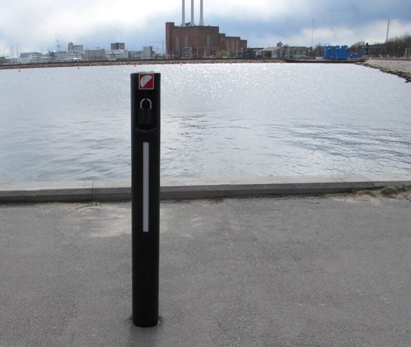 Sort pullert ved havn med industribygning i baggrunden